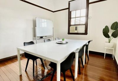 Bright meeting room with a long white table, black chairs, and a whiteboard.