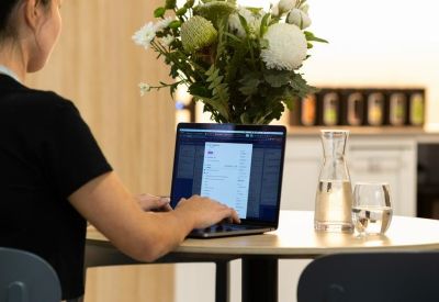 Close-up of a person working on a laptop at a cafe table with a glass of water and flowers.