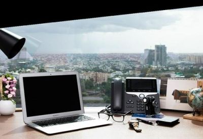Close-up of a modern workstation with a laptop, lamp, and city views.