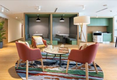 Modern communal lounge area with coral-colored armchairs, a patterned rug, and private wood-paneled booths.