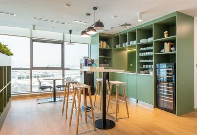 Light-filled kitchen area and breakout space featuring a green feature wall and high-top seating.
