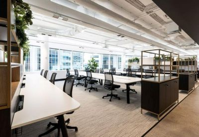 Open-plan office space featuring long white desks, ergonomic chairs, and large windows.