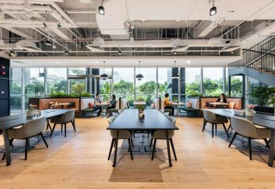 Large open coworking area with long black tables and views of lush greenery through floor-to-ceiling windows.