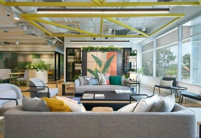 Spacious communal lounge with grey sofas, colorful cushions, and large windows.