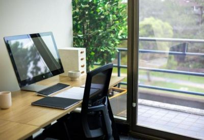 Private office workstation with a large monitor on a wooden desk next to a sunny window.