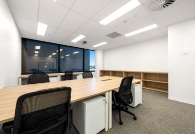 Open-plan office suite with wood-finish desks, black chairs and shelving unit.