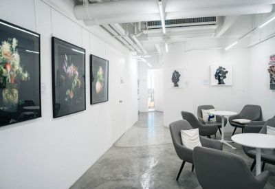 Modern communal lounge with grey armchairs, white tables, and framed floral artwork.