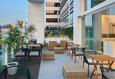 Sunny outdoor rooftop terrace with wicker lounge furniture and wooden tables.
