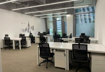 Open-plan office space featuring white desks, ergonomic black chairs, and large windows.