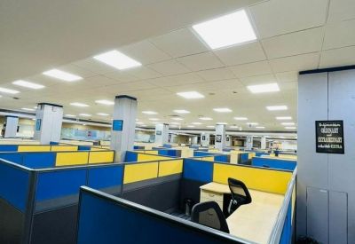 Modern open-plan office with blue and yellow cubicles and bright LED panel lighting.