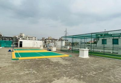 Outdoor rooftop sports area with green badminton courts and a cricket net.