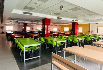 Spacious communal cafeteria with vibrant green chairs and red structural pillars.