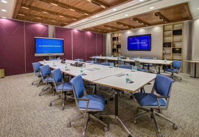 Large conference room with two long white tables, blue chairs, and multiple video screens.