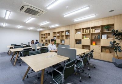 Open-plan office space with light wood desks, ergonomic chairs, and large built-in bookshelves.