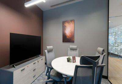 Small meeting room with a round table, grey chairs, and a wall-mounted television.