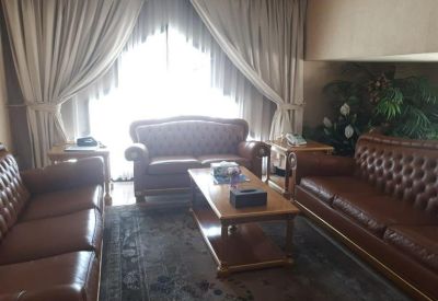 Bright executive office with a large wooden desk, leather chairs, and a seating area in the background.