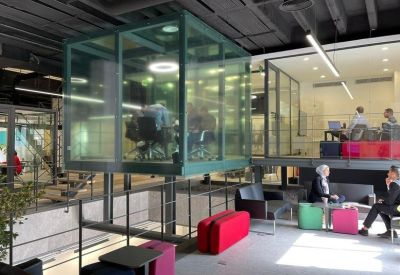Modern coworking space with a central glass meeting cube and colorful modular seating.