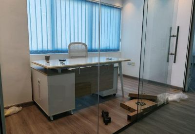 Executive desk behind a glass partition with blue vertical blinds.