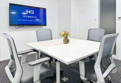 Bright meeting room with a white square table, ergonomic grey chairs, and a wall-mounted TV.