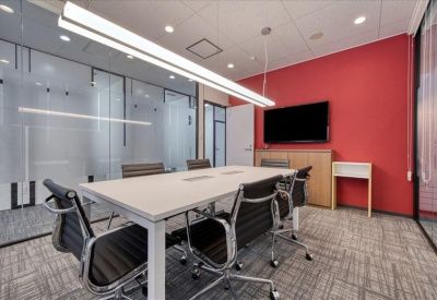 Bright conference room with a large white table, black chairs, and a red feature wall.