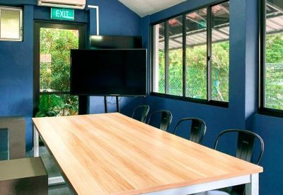 Meeting room with a large wooden table, black chairs, and a television screen against blue walls.