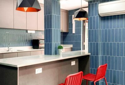 Modern kitchen and breakroom featuring blue tiled walls, red stools, and geometric pendant lights.