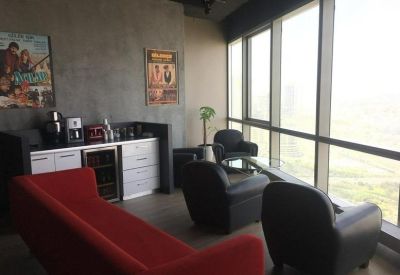 Sunlit communal lounge with a red sofa, black armchairs, and a coffee station overlooking the city.