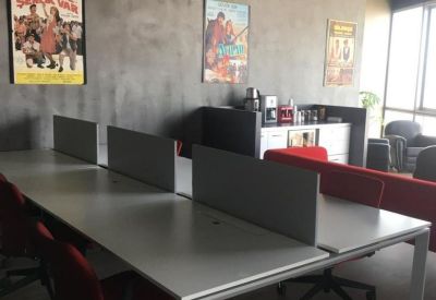 Open-plan office area with long white desks, red chairs, and grey industrial-style walls.
