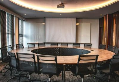 Modern boardroom featuring a large circular wooden table and projector screen.
