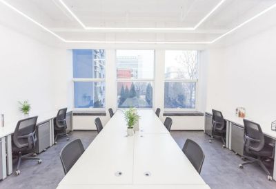 Open-plan office with a long central desk and workstations facing large windows.