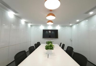Meeting room with a long white table, black chairs, and a wall-mounted screen.