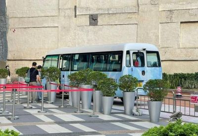 Building shuttle bus waiting area with a blue minibus and potted plants.