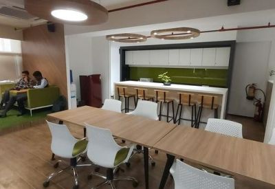 Communal breakout area featuring wooden tables, white chairs, and a small indoor green patch.