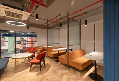 Modern coworking cafe area with orange booth seating and wooden herringbone floors.