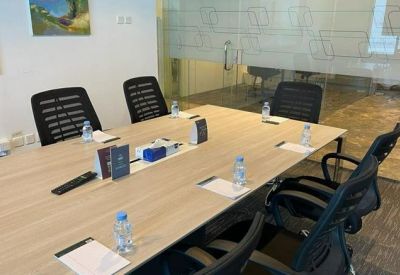 Modern conference room with a light wood table, black mesh chairs, and glass partitions.