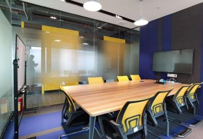 Modern meeting room with a wooden table, yellow chairs, and integrated presentation screen.