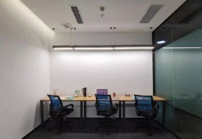 Three-person desk setup against a white wall with ergonomic blue mesh chairs.