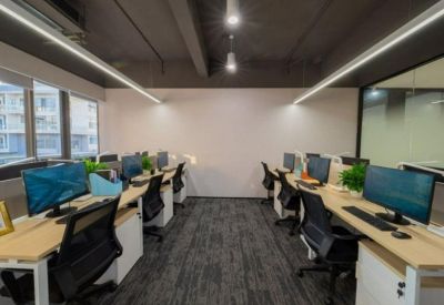 Open-plan office with white workstations, ergonomic black chairs, and dark industrial ceilings.
