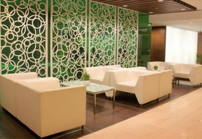 Communal lounge area with white armchairs and a decorative green geometric screen.