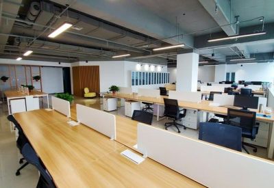 Bright open-plan office with long wooden desks, white partitions, and ergonomic black chairs.