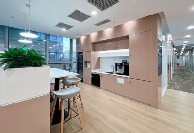 Modern kitchen and breakout area with pink cabinetry, a coffee machine, and high stools.