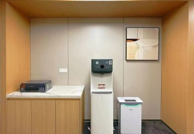 Office refreshment area with a water dispenser, printer, and modern cabinetry under warm recessed lighting.