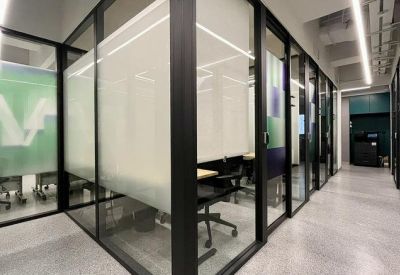 Bright hallway with glass-walled private office suites and frosted privacy panels.