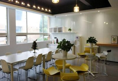 Communal kitchen area with large windows and bright yellow chairs.
