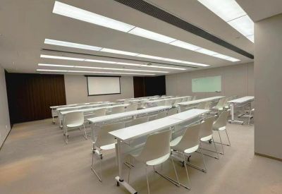 Bright seminar or training room with rows of white desks and chairs facing a projection screen.