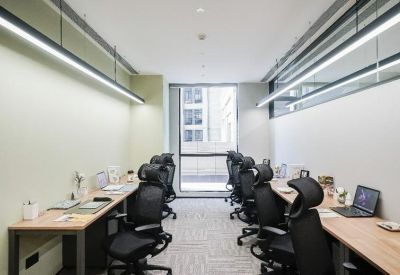 Shared office space with rows of ergonomic black chairs and long wooden desks under linear lights.