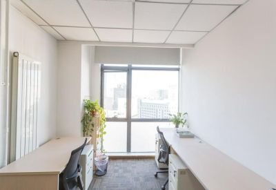 Minimalist private office suite with two white desks and a large window providing natural light.