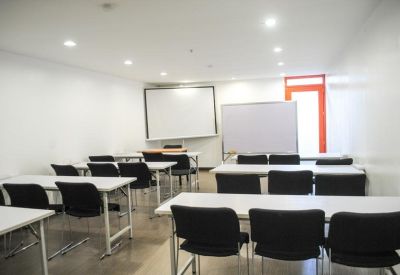 Bright white training room with multiple rows of tables and a projection screen.