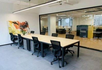 Open-plan workspace with a long shared desk, ergonomic chairs, and a colorful abstract mural.