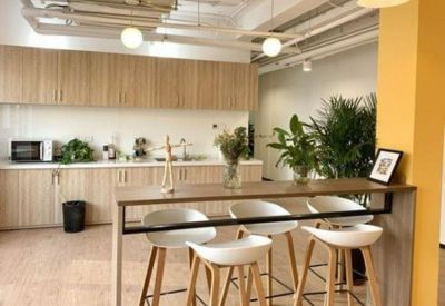 Modern office kitchen and breakout space with wood cabinetry and high-top stools.
